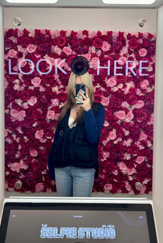 A woman taking a selfie in a photobooth with a rose backdrop